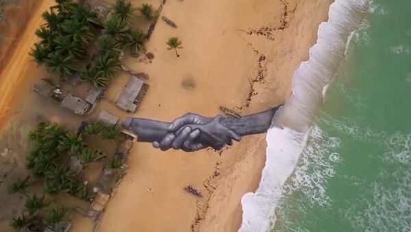 Saype adıyla bilinen Fransız sanatçı Duvarların Ötesi  projesi kapsamında, tuval olarak bu kez Benin'deki bir sahili kullandı. Sanatçı, birbirini sımsıkı tutan devasa el freskiyle, sahile dostluk ve birliktelik mesajı bıraktı. - Sputnik Türkiye