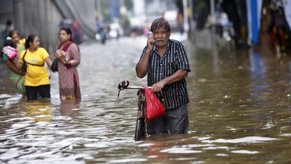 A man talks on his mobile phone while walking though a water logged street during heavy rain in Mumbai, India - Sputnik Türkiye